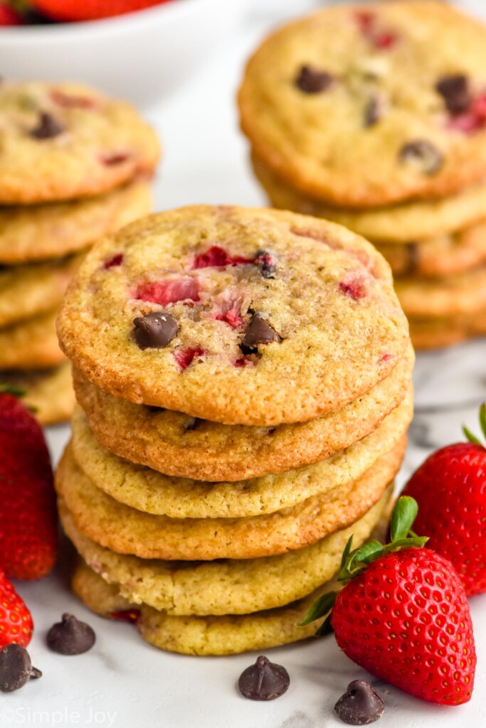 Stack of strawberry cookies with chocolate chips and strawberries sitting beside