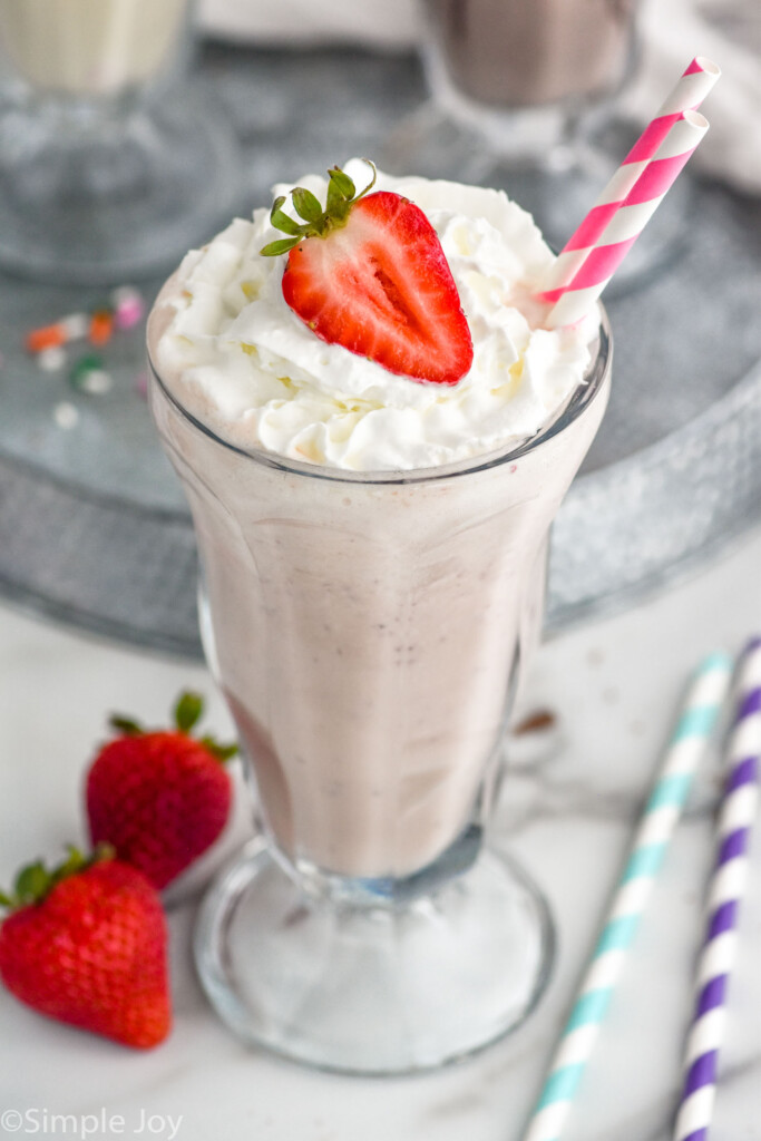 Glass of homemade strawberry milkshake topped with whipped cream, strawberry, and straws