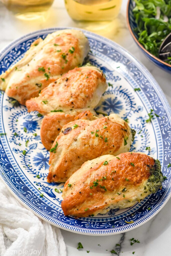 platter of 5 stuffed chicken breasts on a platter. Bowl of arugula salad sitting in background