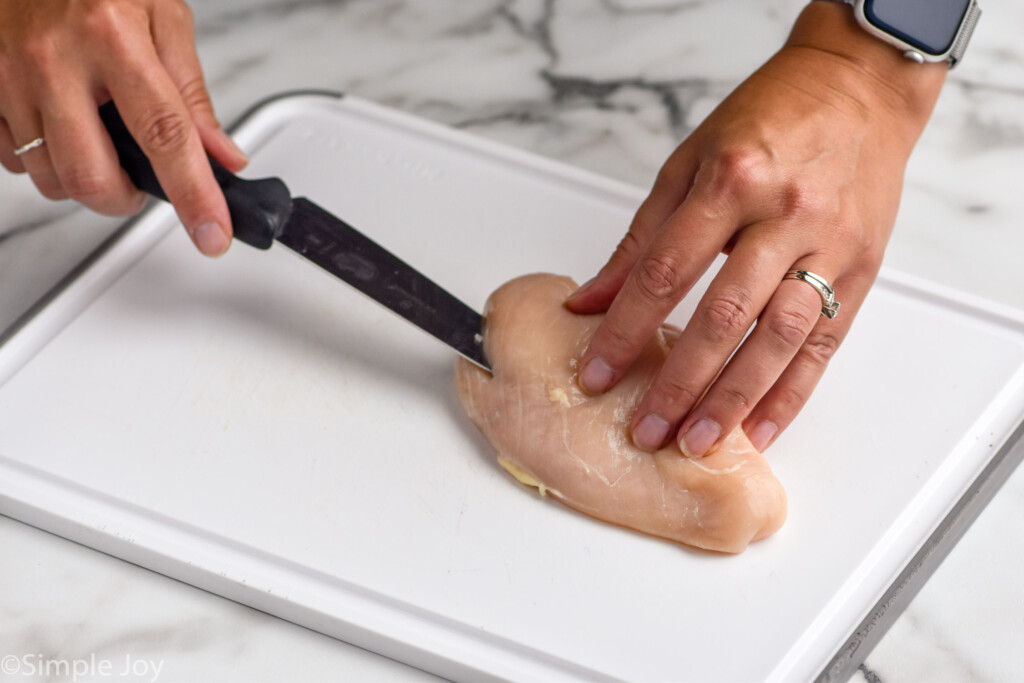 woman cutting raw chicken breast on a cutting board to make stuffed chicken breast