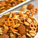 pinterest graphic of close up of a white bowl of Chex mix recipe with some around the bowl, says "the best Chex mix recipe simplejoy.com"