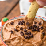 Pinterest graphic for Pumpkin Nutella Dip recipe. Text says, "delicious Pumpkin Nutella Dip simplejoy.com." Image shows person's hand dipping cracker into bowl of Pumpkin Nutella Dip garnished with mini chocolate chips. More dipping sticks beside bowl.