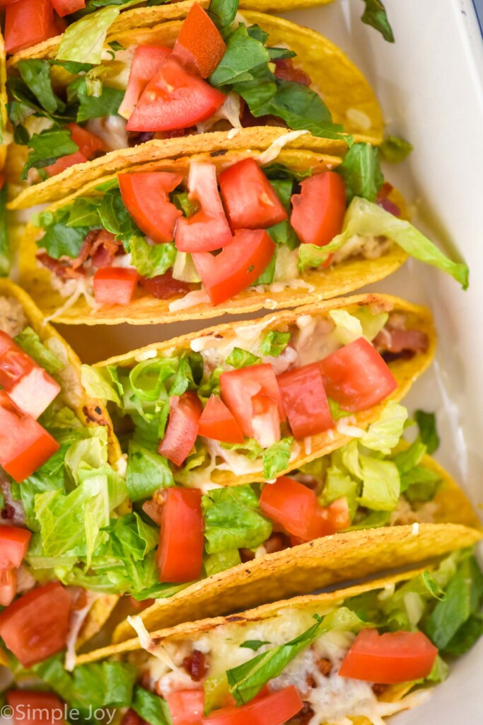 close up of BLT Baked Tacos in a baking dish topped with diced tomatoes and lettuce