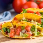 BLT Baked Tacos on a cutting board with tomatoes sitting in background