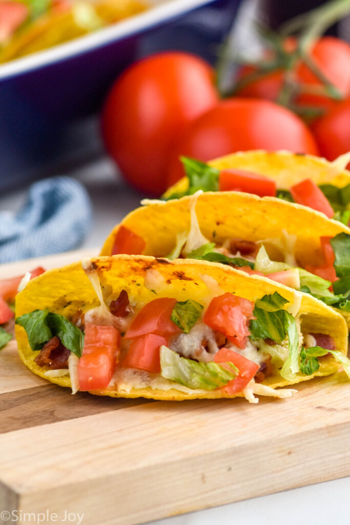 BLT Baked Tacos on a cutting board with tomatoes sitting in background