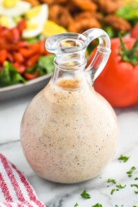 Glass jar of homemade Cajun Ranch Dressing with salad and tomatoes sitting in background