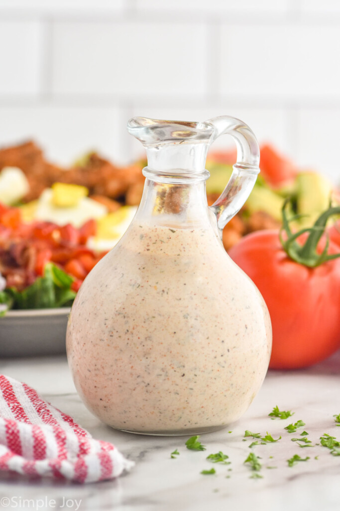 Glass jar of homemade Cajun Ranch Dressing with salad and tomatoes sitting in background