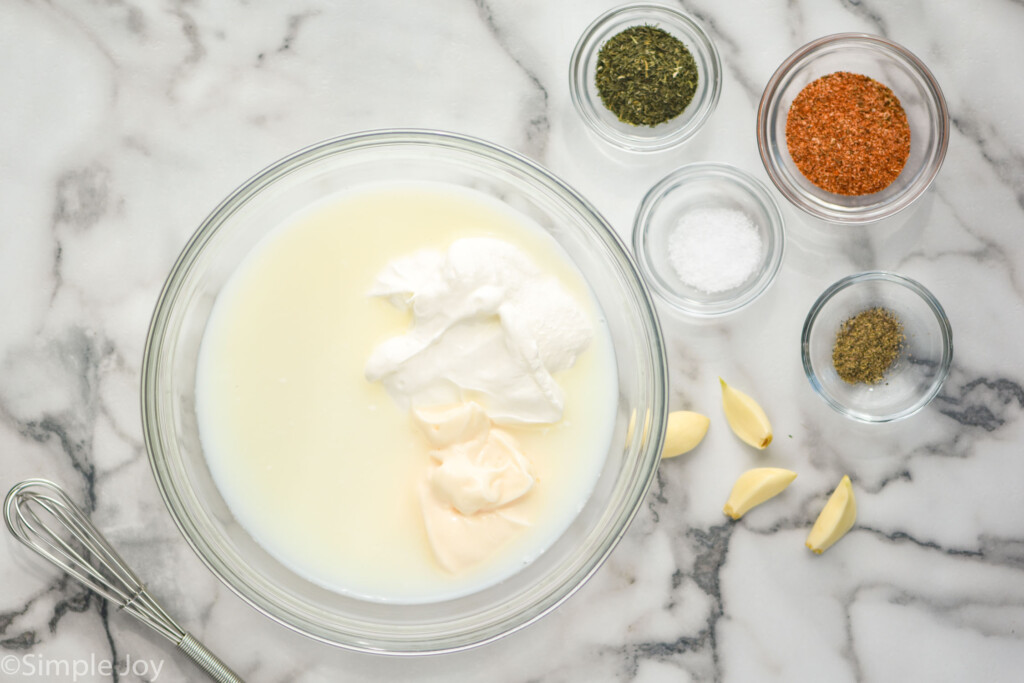 overhead of bowls of Cajun Ranch Dressing ingredients and fresh garlic with a whisk for mixing