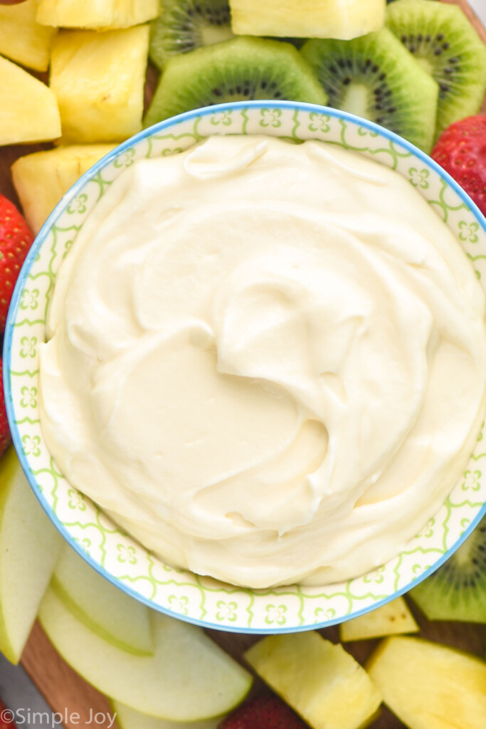 overhead of bowl of Fruit Dip surrounded by fresh kiwi, pineapple, apples, and strawberries