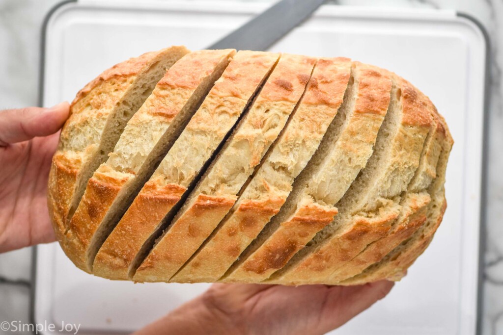 man's hands holding loaf of bread that has been cut to make Pull Apart Bread. Cutting board and knife underneath