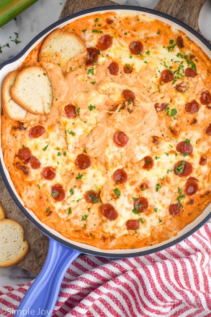 overhead of skillet of Pizza Dip topped with pepperoni and fresh parsley, pieces of toasted baguette on the side