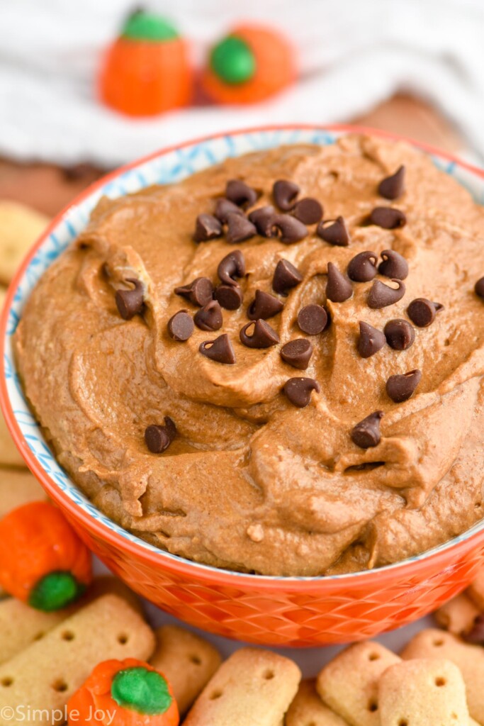 Bowl of Pumpkin Nutella Dip garnished with mini chocolate chips. Dipping crackers and candy pumpkins beside.