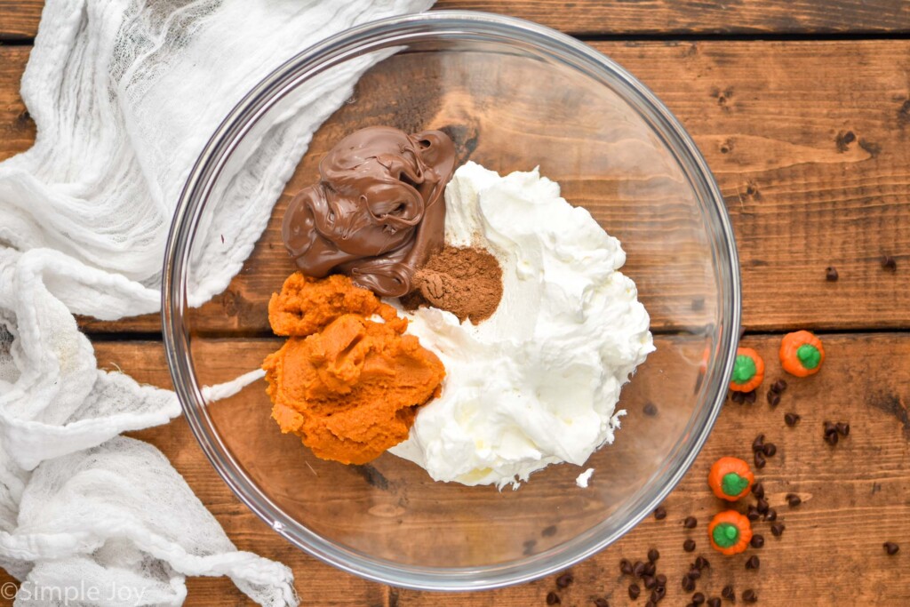 Overhead view of a clear mixing bowl of ingredients for Pumpkin Nutella Dip recipe.