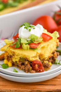 piece of Tamale Pie on a plate topped with sour cream, shredded lettuce, and chopped tomatoes