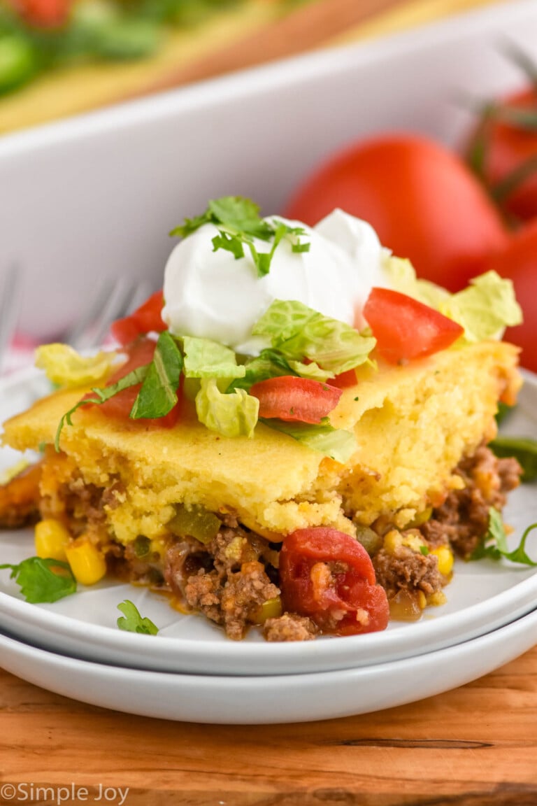 piece of Tamale Pie on a plate topped with sour cream, shredded lettuce, and chopped tomatoes