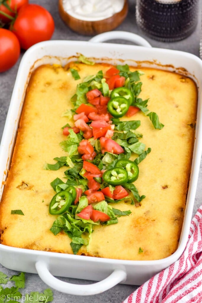 Casserole dish of Tamale Pie topped with diced tomatoes, lettuce, jalapenos