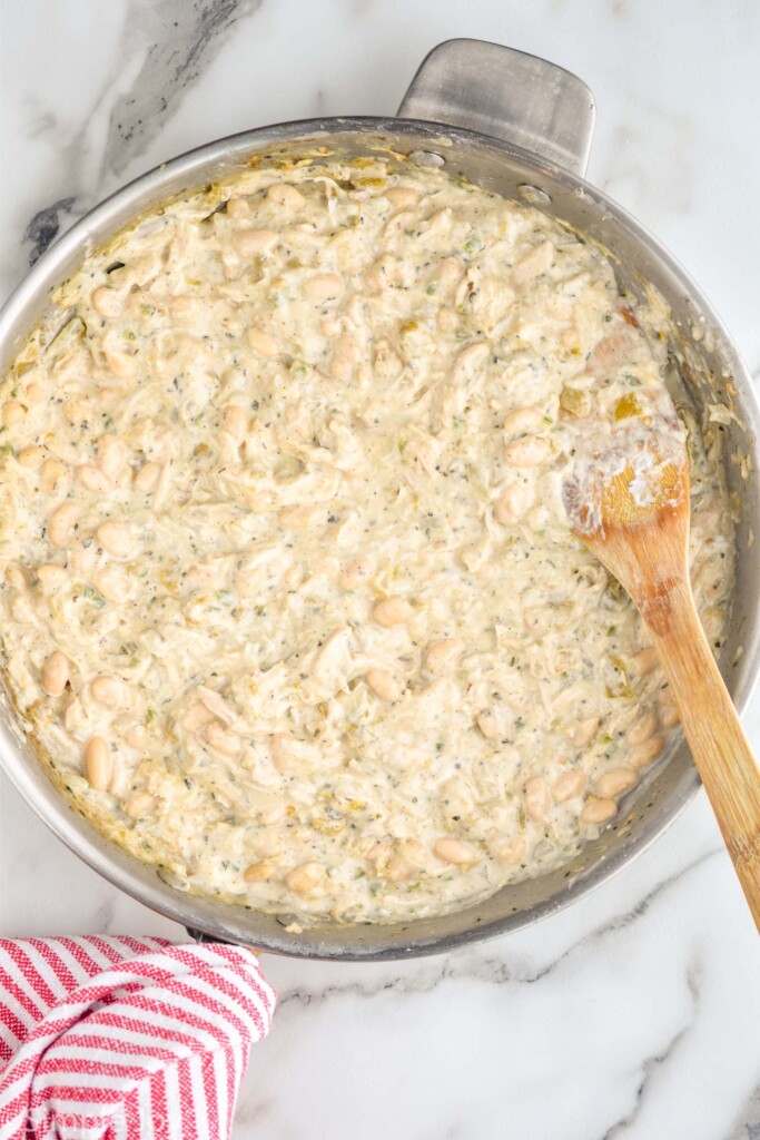 overhead of stainless steel skillet of White Chicken Chili Stuffed Peppers filling ingredients with wooden spoon