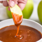 Pinterest graphic for caramel apple dip. Text says "the best caramel dip simplejoy.com" Image shows hand holding apple slice dipped in bowl of caramel dip surrounded by green apple slices