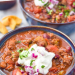 Pinterest graphic for Easy Chili Recipe. Text says "super delicious Easy Chili Recipe simplejoy.com" Image shows a bowl of Easy Chili Recipe topped with sour cream, diced red onion, and fresh cilantro with corn chips sitting beside