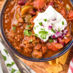 Pinterest graphic for Easy Chili Recipe. Image shows overhead of a bowl of chili topped with sour cream, fresh cilantro, and diced red onion. Text says "super easy easy chili recipe simplejoy.com"