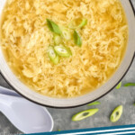 Pinterest graphic for Egg Drop Soup. Image shows overhead of Egg Drop Soup topped with diced green onion, spoon sitting beside bowl. Says "Egg Drop Soup simplejoy.com"