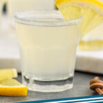 Pinterest graphic for Lemon Drop Shot. Image shows a Lemon Drop Shot in a shot glass with sugared rim and garnished with a lemon slice. Lemon Drop Shots sitting in background. Text says "Lemon Drop Shot simplejoy.com"