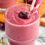 angled view of a cherry smoothie in a glass with a cherry on top and two paper straws