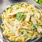 plate of Chicken Broccoli Alfredo topped with shredded parmesan cheese. Glass of wine and bowl of salad sitting beside