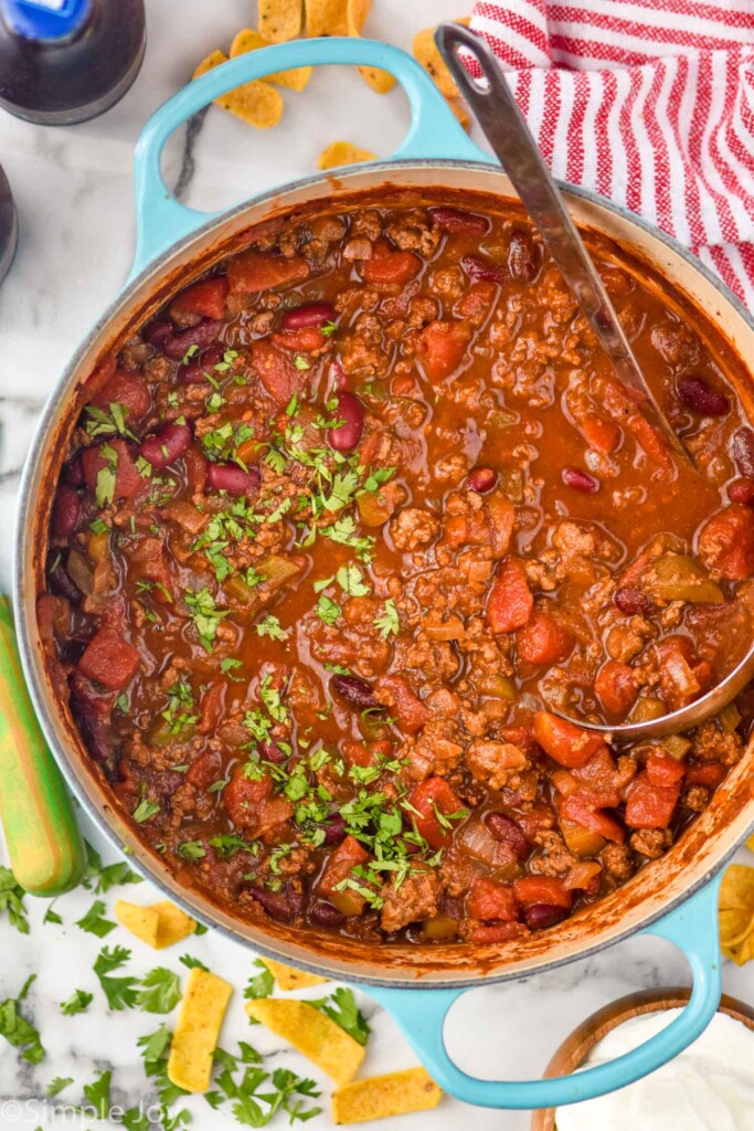 overhead of large pot of chili with fresh parsley and a ladle with corn chips and parsley sitting beside.