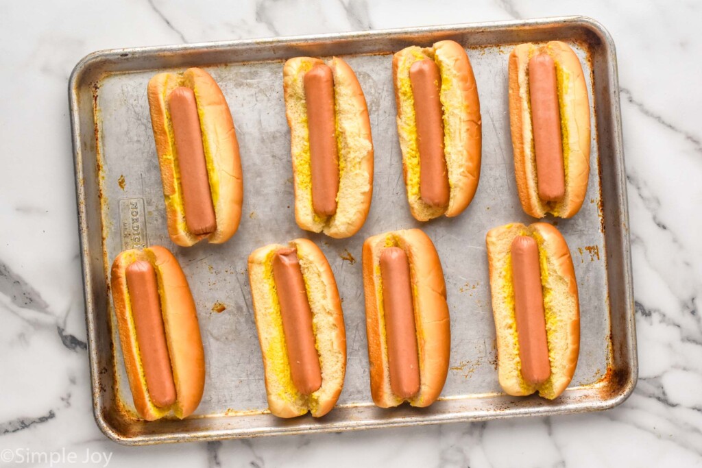 overhead of baking sheet of hot dog buns with hot dogs to make Chili Dogs