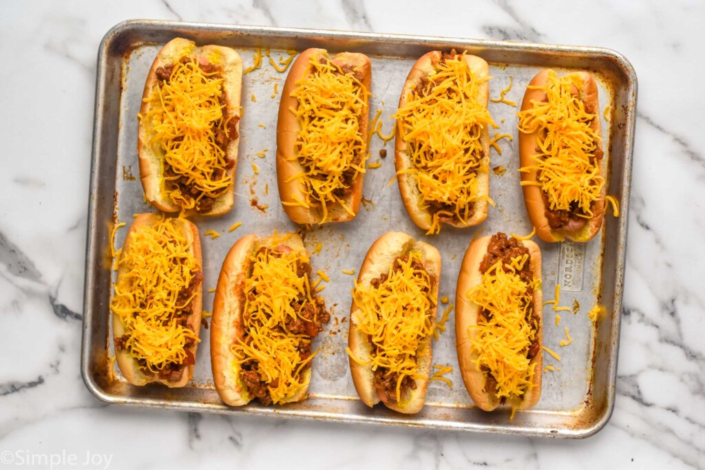 overhead of baking sheet of Chili Dogs topped with shredded cheddar cheese