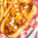 Chili Dogs topped with diced onion with french fries sitting beside