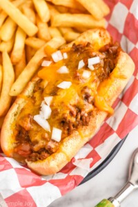 Chili Dogs topped with diced onion with french fries sitting beside