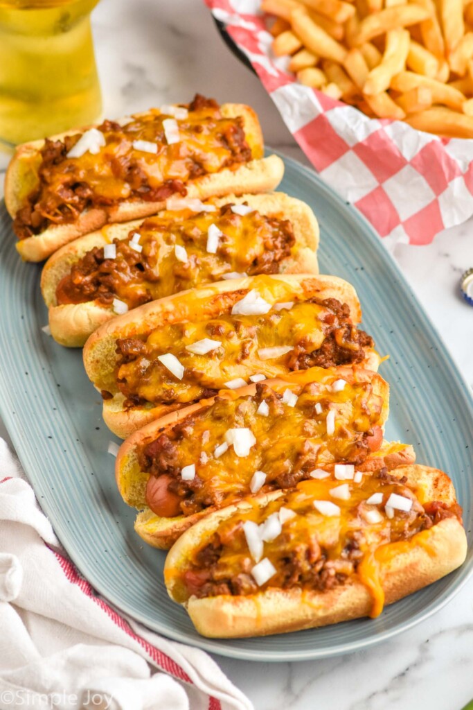 plate of Chili Dogs topped with onions. Plate of french fries sitting in background