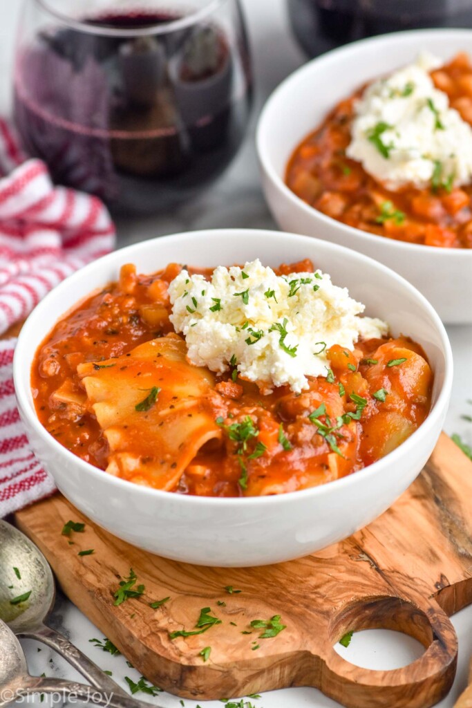 bowl of Lasagna Soup topped with cheese mixture and fresh parsley. Bowl of Lasagna Soup and glass of red wine sitting in background