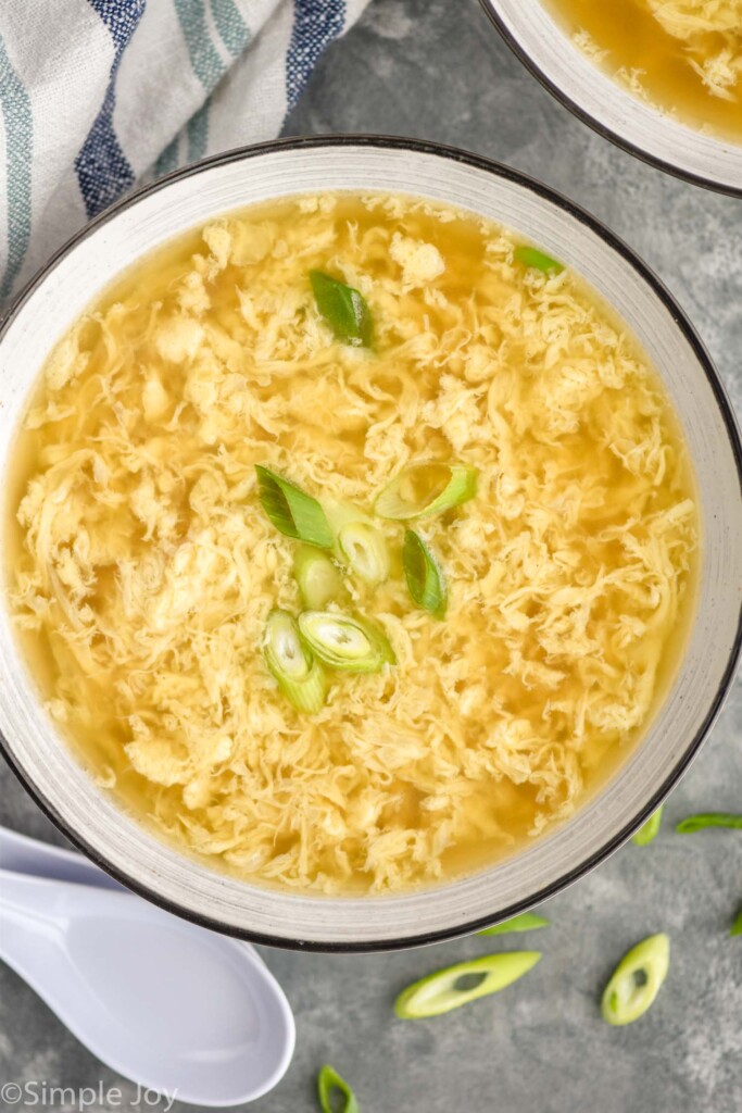 Overhead of bowl of Egg Drop Soup topped with green onion with spoon sitting beside