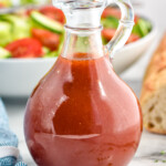 Jar of homemade French Dressing with bowl of salad and baguette sitting in background