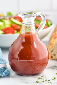 Jar of homemade French Dressing with bowl of salad and baguette sitting in background