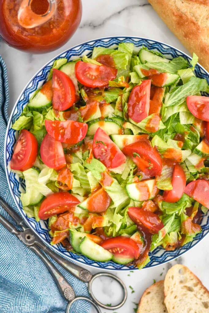 overhead of bowl of lettuce salad with tomato slices and french dressing