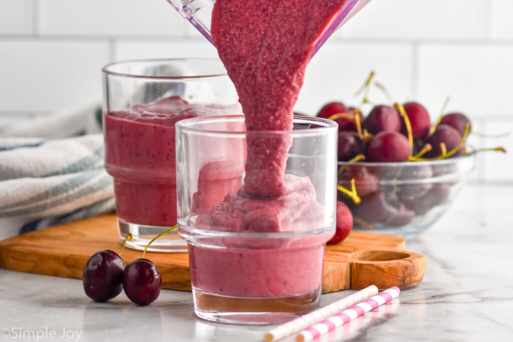 cherry smoothie being poured into a glass from a blender