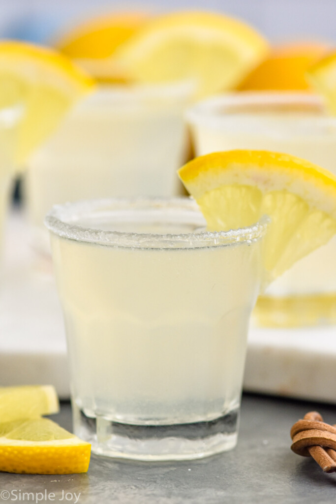 Lemon Drop Shot in a shot glass with sugar on the rim and a slice of lemon for garnish. Lemon slices sitting beside