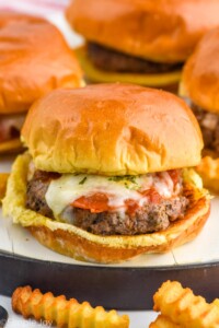 Pizza Burger on a bun with melted cheese and pepperoni. French fries sitting in front, Pizza Burgers sitting in background