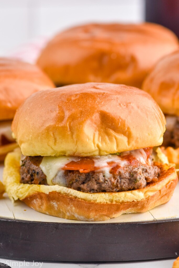 Pizza burger on a bun with cheese and pepperoni on a bun with other Pizza Burgers sitting behind