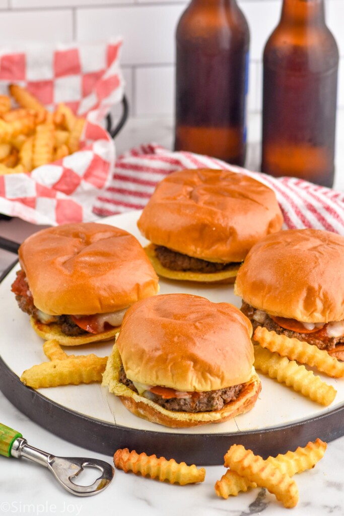 four Pizza Burgers on buns surrounded by french fries. Two bottles of beer and a basket of french fries sitting in background