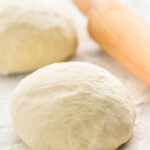 Two balls of Pizza Dough and rolling pin on flour-covered surface.