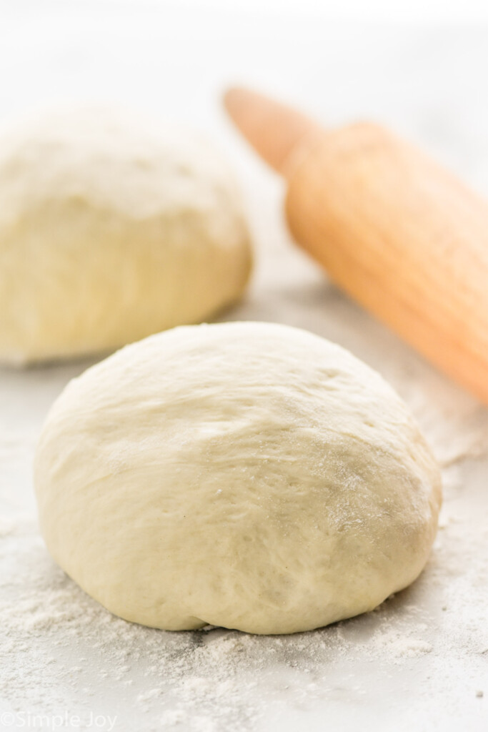 Two balls of Pizza Dough and rolling pin on flour-covered surface.