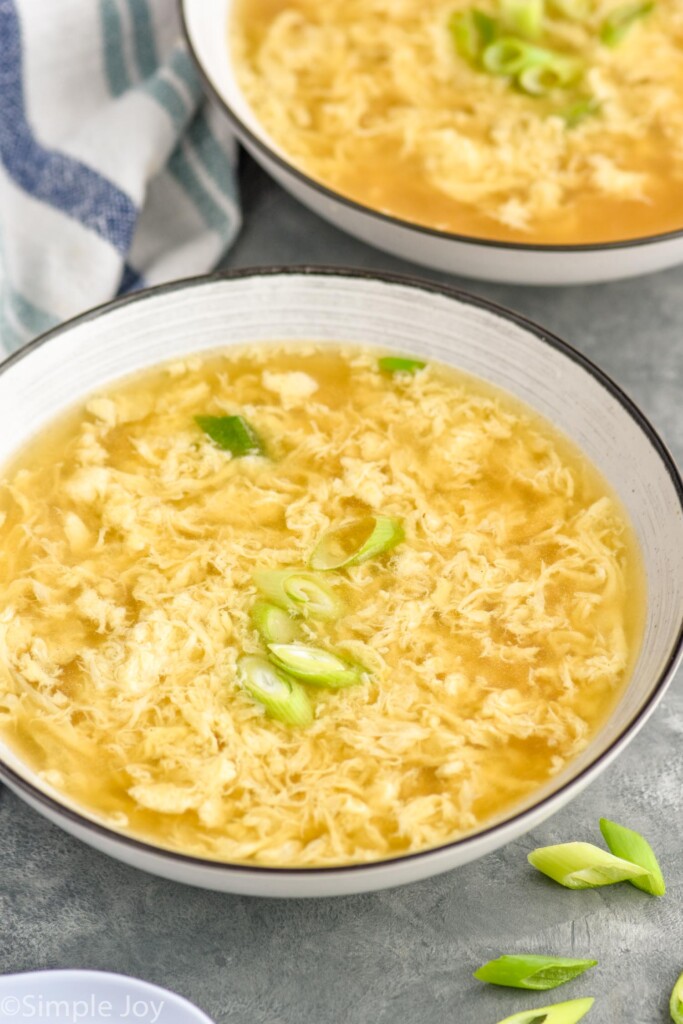 bowl of Egg Drop Soup topped with diced green onions with another bowl of Egg Drop Soup sitting behind