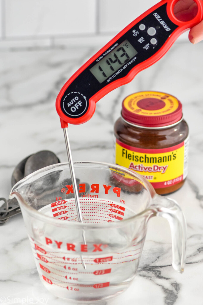 Photo of an instant read thermometer in a measuring cup of water with yeast beside for Pizza Dough recipe.