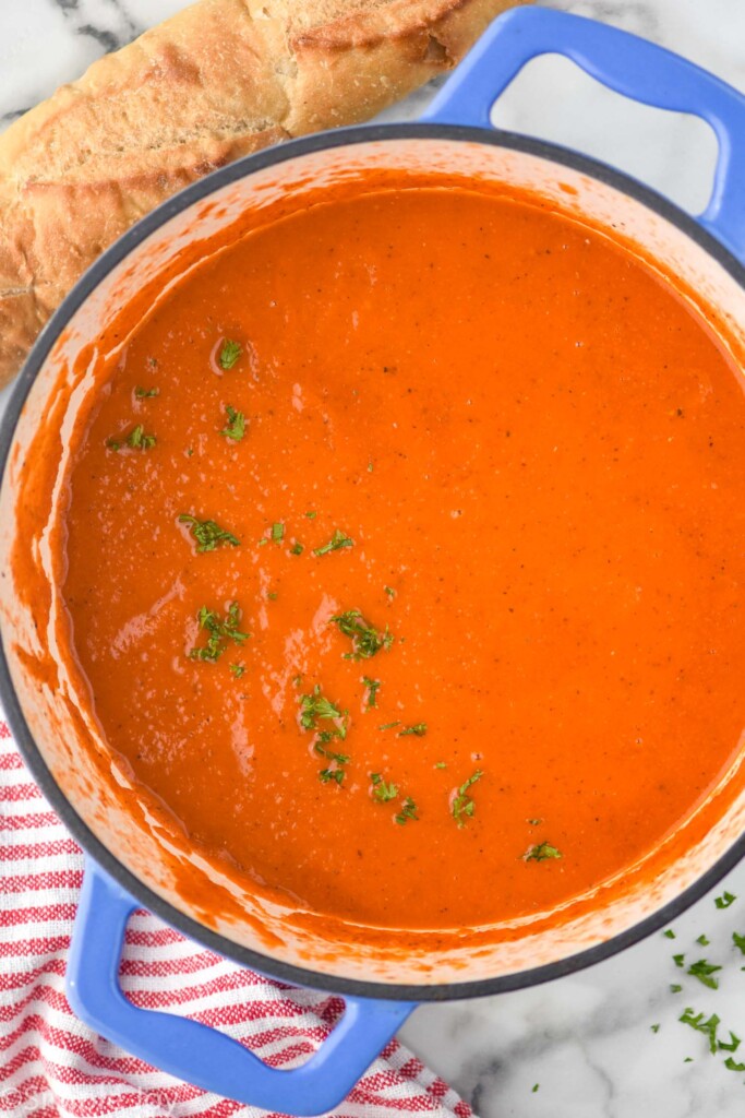 Overhead view of a pot Tomato Soup garnished with parsley. Loaf of bread beside.