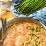 Pinterest graphic for Lemon Chicken. Text says "delicious Lemon Chicken simplejoy.com" Image shows a skillet of Lemon Chicken with fresh parsley and two forks. Plate of asparagus and glass of white wine sitting behind